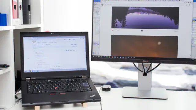 Laptop i monitor na biurku z otwartymi panelami danych