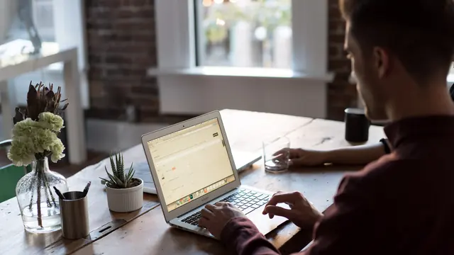 Mężczyzna pracujący na laptopie przy drewnianym biurku w jasnym biurze