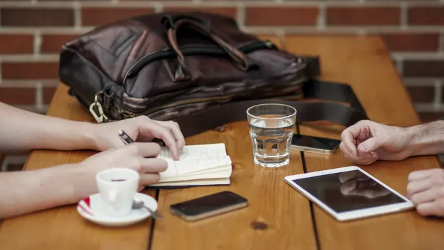 Dwie osoby przy stole ze skórzaną torbą, notatkami, tabletem i kawą