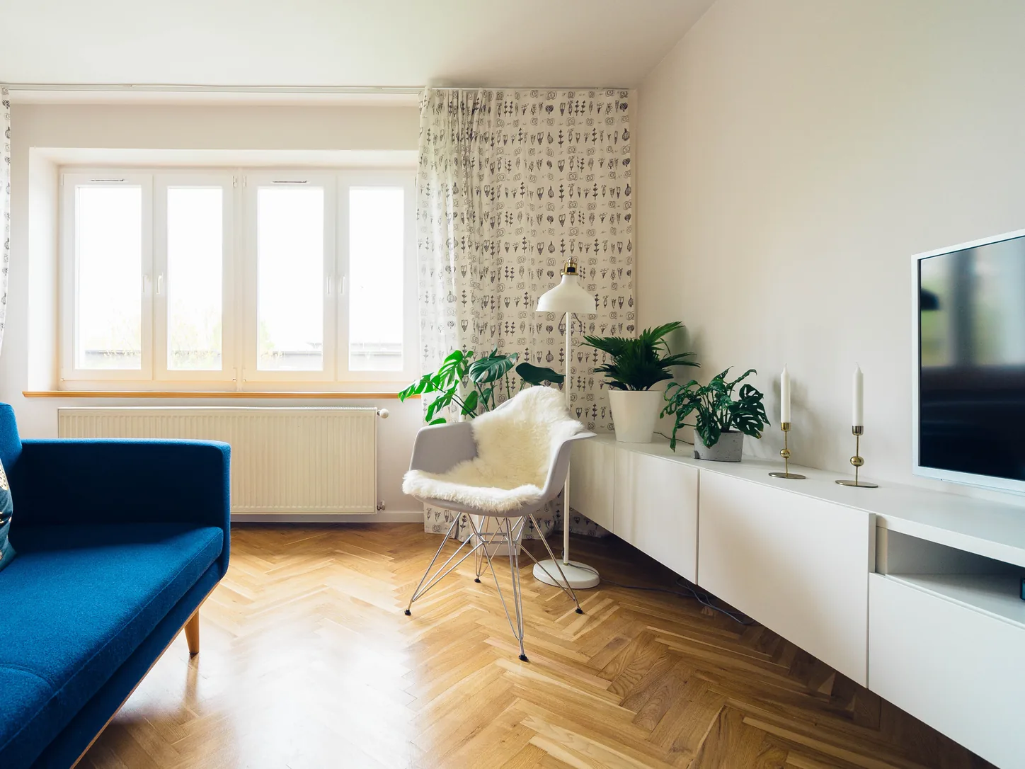 Jasny salon w mieszkaniu: niebieska sofa, parkiet w jodełkę i duże okno